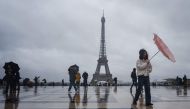 A tourist tries to protect herself with an umbrella on a rainy day at the Esplanade du Trocadero with the Eiffel Tower in the background, which is closed to the public on the fourth day of its staff's strike, in Paris on February 22, 2024. Photo by Dimitar DILKOFF / AFP