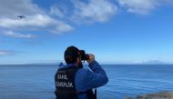 :This handout photograph taken and released on March 15, 2024 in Canakkale by Turkish news agency DHA (Demiroren News Agency) shows a coast guard officer looking through binoculars as a drone seaches for victims, after at least eight migrants drowned after a boat carrying them capsized off the Turkish coast in the Aegean Sea. (Photo by Demiroren News AAgency / DHA (Demiroren News Agency) / AFP)
