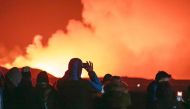 People gather to watch as molten lava flows out from a fissure on the Reykjanes peninsula north of the evacuated town of Grindavik, western Iceland on March 16, 2024 Photo Credit: Ael Kermarec / AFP.