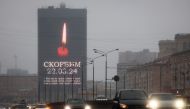 Cars drive past an advertising screen on the facade of a building displaying an image of a lit candle and the slogan 
