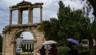 File: Tourists holding umbrellas walk in front of the ancient Roman Andrian Gate, during a hot day in Athens on June 13, 2024. (Photo by Aris Messinis / AFP)

