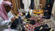 Saudi tailor Habib Mohammed (L) his grandson Ghassan and his granddaughter Fajr, work on bishts, inside Mohammed's workshop in the oasis city of Hofuf, in Saudi Arabia on February 16, 2025. (Photo by Fayez Nureldine / AFP)
