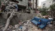 A Palestinian boy sits on a damaged couch as he watches people clearing the rubble from a house hit in Israeli strikes at the Nuseirat refugee camp. (Photo by Eyad BABA / AFP)