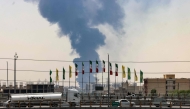 Flags flutter along a bridge as a plume of heavy smoke and fire rise from an oil refinery in southern Tehran, after it was hit in an overnight Israeli strike, on June 15, 2025.  (Photo by Atta Kenare / AFP)
 