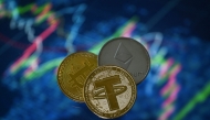 (Files) An illustration picture taken in London on May 8, 2022, shows gold plated souvenir cryptocurrency Tether (USDT), Bitcoin and Etherium coins arranged beside a screen displaying a trading chart. (Photo by Justin Tallis / AFP)