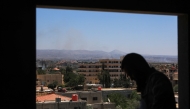 A man stands at a window as smoke billows during Israeli strikes in the vicinity of Syria's southern city of Sweida on July 16, 2025. Photo by Bakr ALKASEM / AFP