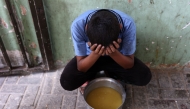 A displaced Palestinian child sits next to a pot of lentil soup that he received at a food distribution point in Gaza City in the northern Gaza Strip on July 25, 2025. (Photo by Omar AL-QATTAA / AFP)
