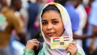 A woman holds a card depicting the flags of Egypt and Sudan and with the Arabic text 