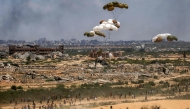 Palestinians rush to the scene as aid pallets are parachuted after being dropped from a military plane over Nuseirat in the central Gaza Strip on August 5, 2025. (Photo by Eyad Baba / AFP)