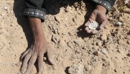 A Palestinian woman searches the sand for legumes or rice in Nuseirat in the central Gaza Strip during an airdrop mission on August 5, 2025. (Photo by Eyad Baba / AFP)