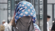 A pedestrian wears a cloth over her head to protect herself from the heat and sun on a hot day in Tokyo on August 5, 2025. (Photo by Kazuhiro Nogi / AFP)