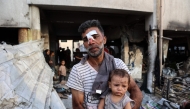 An injured man carries a toddler as others search for their belongings amid the rubble, in the al-Farabi school turned shelter for displaced Palestinians, after it was hit by an Israeli strike, in Gaza City in the northern Gaza Strip on September 7, 2025. (Photo by Omar AL-QATTAA / AFP)