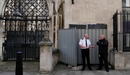 Security guards stand beside a metal barrier covering up an artwork by street artist Banksy, depicting a judge using a gavel to beat a protester using a placard as protection, on an exterior wall of the Royal Courts of Justice in London, on September 8, 2025. (Photo by Carlos Jasso / AFP)