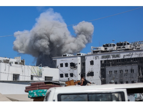 Displaced Palestinians sitting in the back of a truck laden with their belongings while fleeing bombardment, watch smoke billowing amid Israeli strikes on Al-Shati camp for Palestinian refugees west of Gaza City on September 18, 2025. (Photo by Omar Al-Qattaa / AFP)
