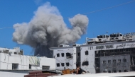Displaced Palestinians sitting in the back of a truck laden with their belongings while fleeing bombardment, watch smoke billowing amid Israeli strikes on Al-Shati camp for Palestinian refugees west of Gaza City on September 18, 2025. (Photo by Omar Al-Qattaa / AFP)
