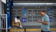 A woman (L) reads a book at a self-service library beside a pavement in Beijing on September 22, 2025. (Photo by WANG Zhao / AFP)