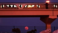 The full moon rises on the horizon as a metro train passes in Doha on October 7, 2025. (Photo by Karim Jaafar / AFP)