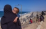 A Palestinian woman holding a child watches people walking along Al-Rashid road toward Gaza City from Nuseirat in the central Gaza Strip on October 10, 2025. (Photo by Bashar Taleb / AFP)