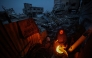 A displaced Palestinian woman warms herself beside a fire amid the ruins of destroyed buildings in the Bureij refugee camp, in the central Gaza Strip, on November 29, 2025. (Photo by Eyad Baba / AFP)
