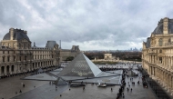 (Files) This photograph shows visitors, seen from the Sully wing, queuing in the Cour Napoleon by the pyramid, to enter the Louvre Museum in Paris on November 19, 2025. (Photo by Sébastien Dupuy / AFP)