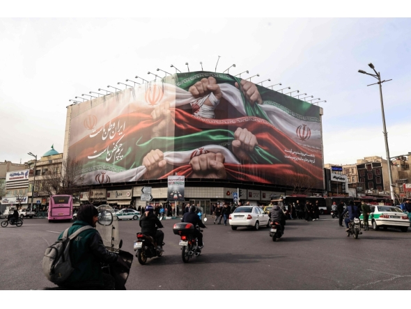 Vehicles pass by a large patriotic banner depicting the Iranian flag in Tehran on January 14, 2026. (Photo by Atta Kenare / AFP)