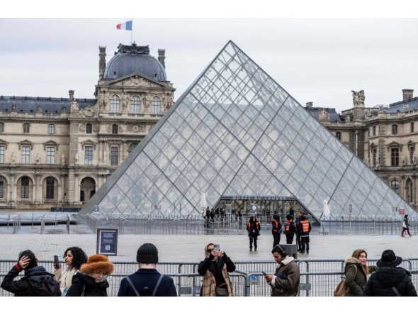 Tourists stand behind barriers blocking the access to the Louvre main courtyard, La Cour Napoleon, with the Louvre Pyramid, designed by Chinese-US architect Ieoh Ming Pei, as the Louvre Museum is closed due a strike, in Paris, on January 12, 2026. Photo by Martin LELIEVRE / AFP