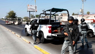 National Guard members stand guard near a burnt bus set on fire by organised crime groups in response to an operation in Jalisco to arrest a high-priority security target, at one of the main avenues in Zapopan, state of Jalisco, Mexico, on February 22, 2026. (Photo by Ulises RUIZ / AFP)
