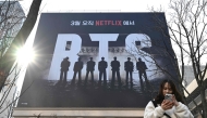 A woman uses her smartphone in front of a billboard promoting a comeback concert of K-pop boy group BTS at Gwanghwamun Square in Seoul on March 17, 2026. (Photo by Jung Yeon-je / AFP)
 