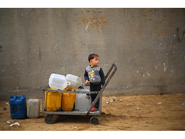 A displaced Palestinian boy stands on a trolley loaded with empty water canisters at the Nuseirat refugee camp, in the central Gaza Strip on April 1, 2026. (Photo by Eyad Baba / AFP)