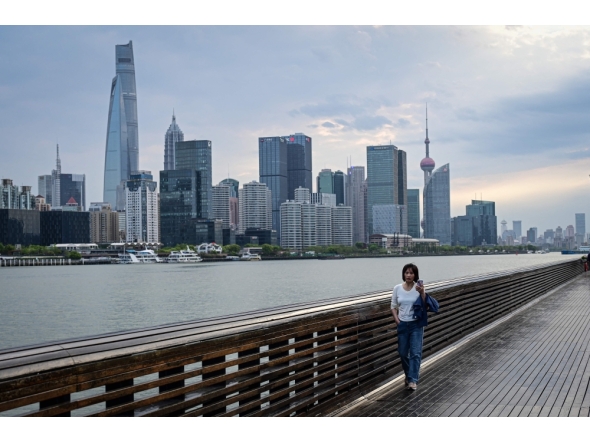 A woman walks along the Huangpu River as the city's skyline is seen in the background in Shanghai on April 9, 2026. (Photo by Jade Gao / AFP)