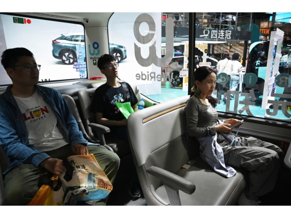 Visitors try out a WeRide autonomous vehicle at the Beijing Auto Show in Beijing on April 26, 2026. (Photo by Greg Baker / AFP)