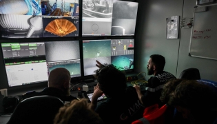 Pilots specializing in underwater robots from the French Navy, along with researchers, watch live feeds on screens showing the “ROV C 4000,” a remotely operated vehicle manufactured by the French company LD Travocean and designed for seabed exploration, during an archaeological mission on the wreck of the CAMARA 4 from the bridge of the (BSAA) Jason, off the coast of Ramatuel, in southeastern France, April 7, 2026. Photo by Thibaud MORITZ / AFP