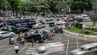 This photograph taken on May 14, 2026 shows commuters waiting to cross a road amid traffic in Dhaka. Photo by Munir UZ ZAMAN / AFP