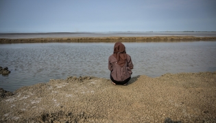 A resident affected by the Lapindo mudflow sits on the embankment in the mud volcano area, marking 20 years since a gas exploration accident triggered a mud flow that inundated more than a dozen villages and permanently displaced tens of thousands of people in Porong, Sidoarjo, East Java province on May 29, 2026. (Photo by JUNI KRISWANTO / AFP)
