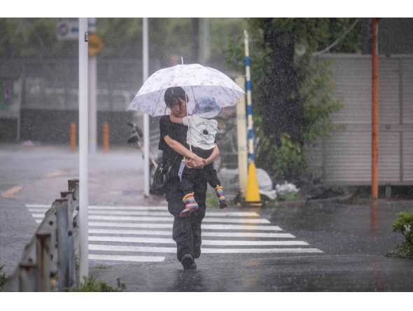 A woman holding her child walks through heavy rain brought by severe tropical storm Jangmi in Tokyo on June 3, 2026. (Photo by Yuichi Yamazaki / AFP)