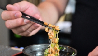 Kenji Suzuki, second-generation owner of Suehiro Japanese Restaurant in Los Angeles, California, lifting natto from a bowl with chopsticks. (Photo by Frederic J. Brown / AFP) 