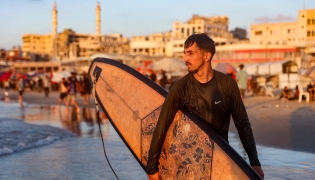 Palestinian surfer Tahseen Abu Assi, 23, takes his surfboard out into the Mediterranean sea off a beach in Gaza City on June 21, 2026. (Photo by Omar Al-Qattaa / AFP)