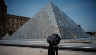A couple protect themselves from the sun under an umbrella in front of the Louvre Pyramid, designed by Chinese-US architect Ieoh Ming Pei in Paris on June 23, 2026, as France experiences a heatwave. (Photo by Dimitar DILKOFF / AFP) 