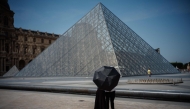 A couple protect themselves from the sun under an umbrella in front of the Louvre Pyramid, designed by Chinese-US architect Ieoh Ming Pei in Paris on June 23, 2026, as France experiences a heatwave. (Photo by Dimitar DILKOFF / AFP) 