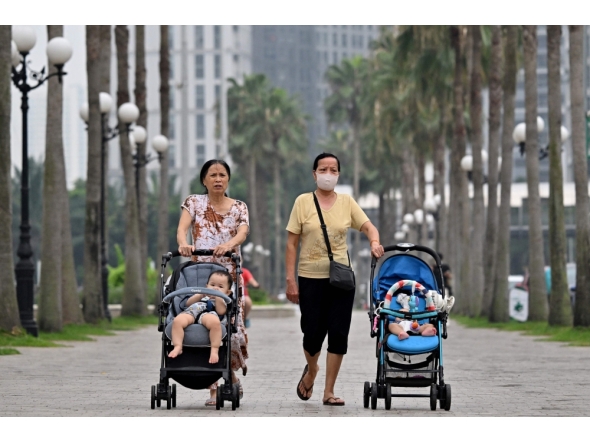 This photo taken on June 29, 2026, shows women pushing strollers with children along a sidewalk in Hanoi. Photo by Nhac Nguyen / AFP
