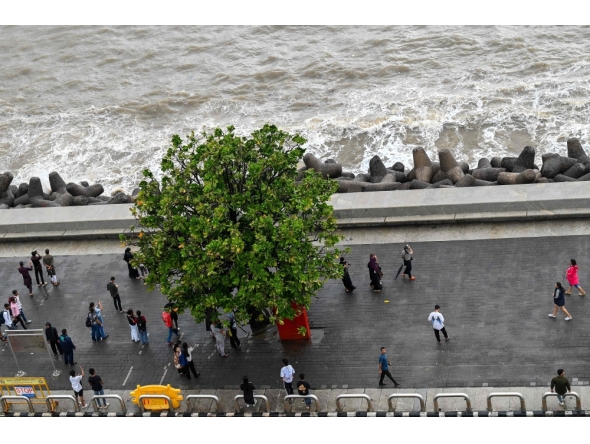 This photograph taken on July 7, 2026 shows pedestrians walking on the footpath along the seafront in Mumbai. (Photo by Punit Paranjpe / AFP)