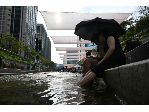 People cool off below sunshades over the Cheonggyecheon Stream in Seoul on August 3, 2026. (Photo by Greg Baker / AFP)
