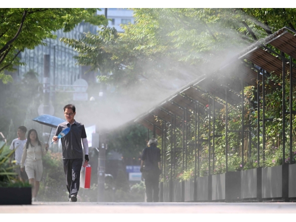 Pedestrians walk along a mist-spraying zone to cool off on a street in Seoul on August 3, 2026, as a scorching heat wave continues to grip South Korea. (Photo by Jung Yeon-je / AFP)