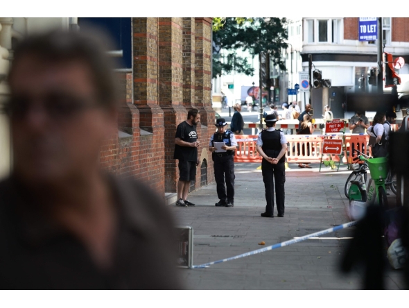 Police community support officers (PCSOs) speak to a person near cordon tape at Endell road in covent garden, central London on August 5, 2026. Photo by Henry NICHOLLS / AFP