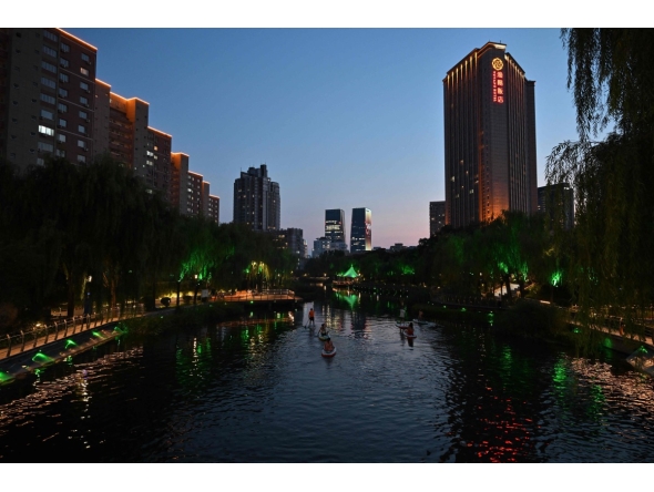 People paddle along the Liangma river at dusk in Beijing on August 5, 2026. (Photo by ADEK BERRY / AFP)