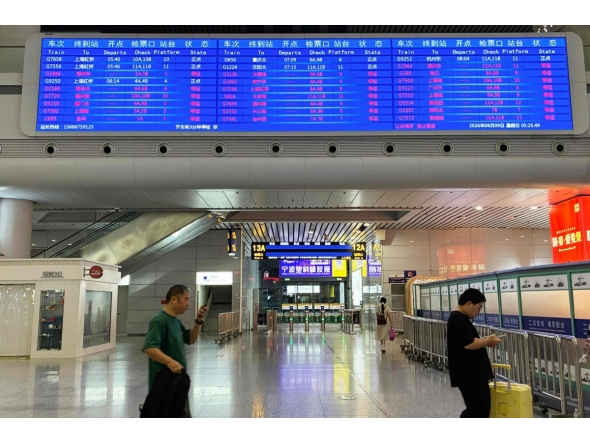 Passengers walk under a departure board at Ningbo railway station as most trains are cancelled due to approaching Typhoon Dolphin on August 9, 2026. (Photo by Rebecca BAILEY / AFP)