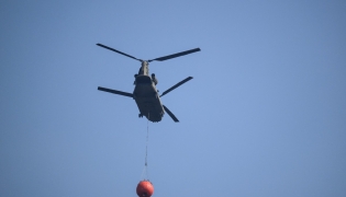 A Royal Netherlands Air Force Boeing CH-47D Chinook carrying a bambi bucket departs from Baelen, near Eupen, eastern Belgium to tackle a wildfire burning in the Hautes Fagnes (High Fens) nature reserve on August 16, 2026. Photo by JOHN THYS / AFP