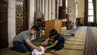 This photo taken on June 6, 2026 shows Kinan Abou Haikal (L), the elder brother of seven-month-old baby Sam Fahd Abou Haikal, sitting next to his body at the Abou Heisheh Mosque in Hebron, in the Israeli-occupied West Bank. (Photo by JOHN WESSELS / AFP)