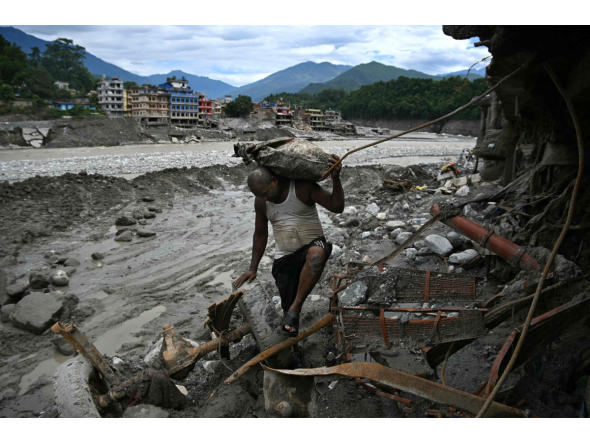 A man carrying his belongings walks past a damaged house in the aftermath of flash floods at Trishuli in Nepal's Nuwakot district on September 11, 2026. (Photo by Prakash MATHEMA / AFP)