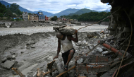 A man carrying his belongings walks past a damaged house in the aftermath of flash floods at Trishuli in Nepal's Nuwakot district on September 11, 2026. (Photo by Prakash MATHEMA / AFP)